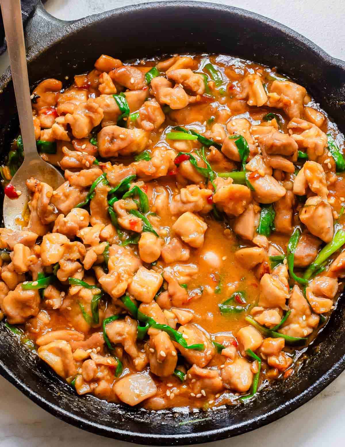 Korean inspired gochujang chicken in a cast iron skillet with a metal serving spoon.