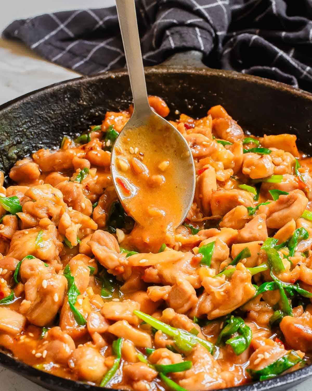 Spooning gochujang sauce over chicken thighs in a skillet.