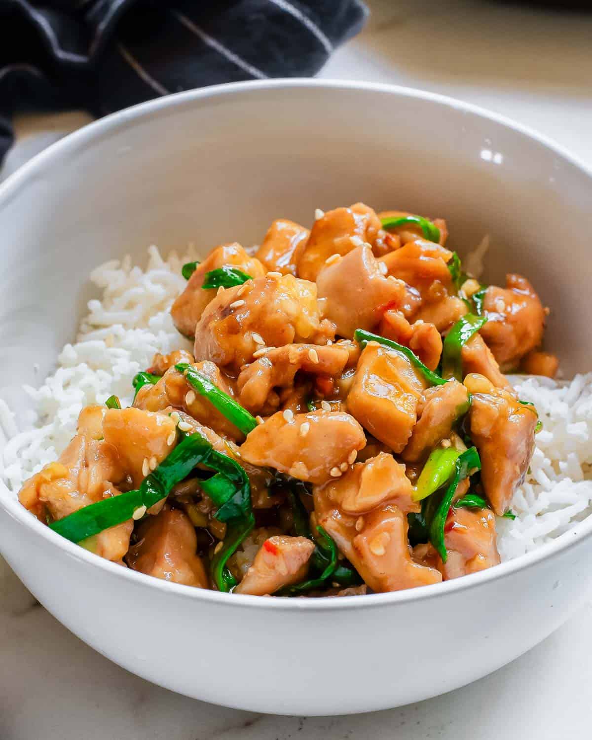 A white bowl with red chili paste gochujang chicken and green onions over white rice.