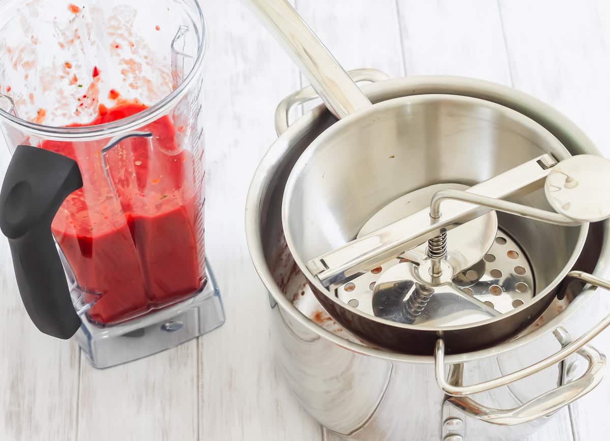 A blender with a v8 juice next to a pot with a food mill.