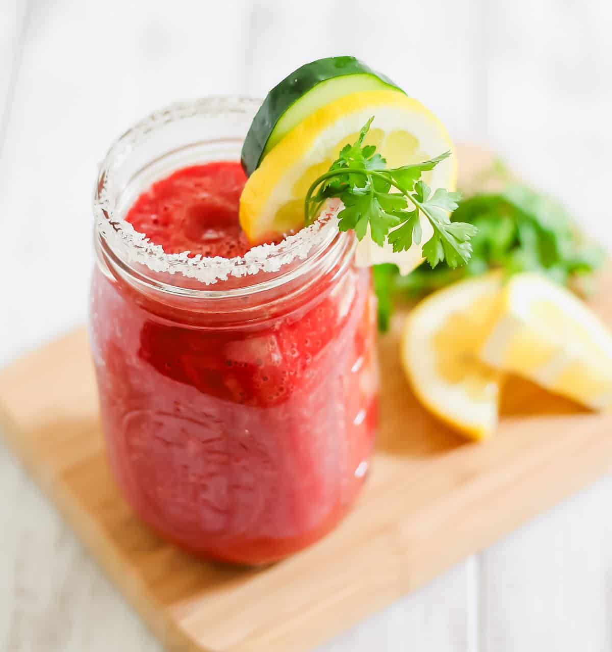 A mason jar filled with homemade V8 juice garnished with a salt rim and a slice of lemon and cucumber.