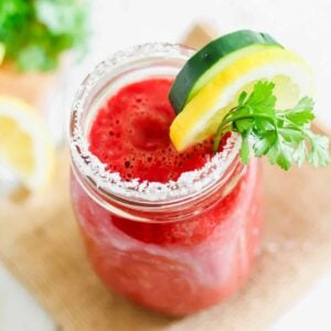 Copycat V8 juice recipe poured into a mason jar lined with salt and garnished with parsley, lemon and cucumber.