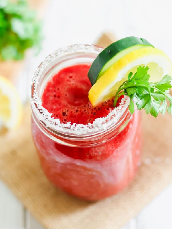 Copycat V8 juice recipe poured into a mason jar lined with salt and garnished with parsley, lemon and cucumber.