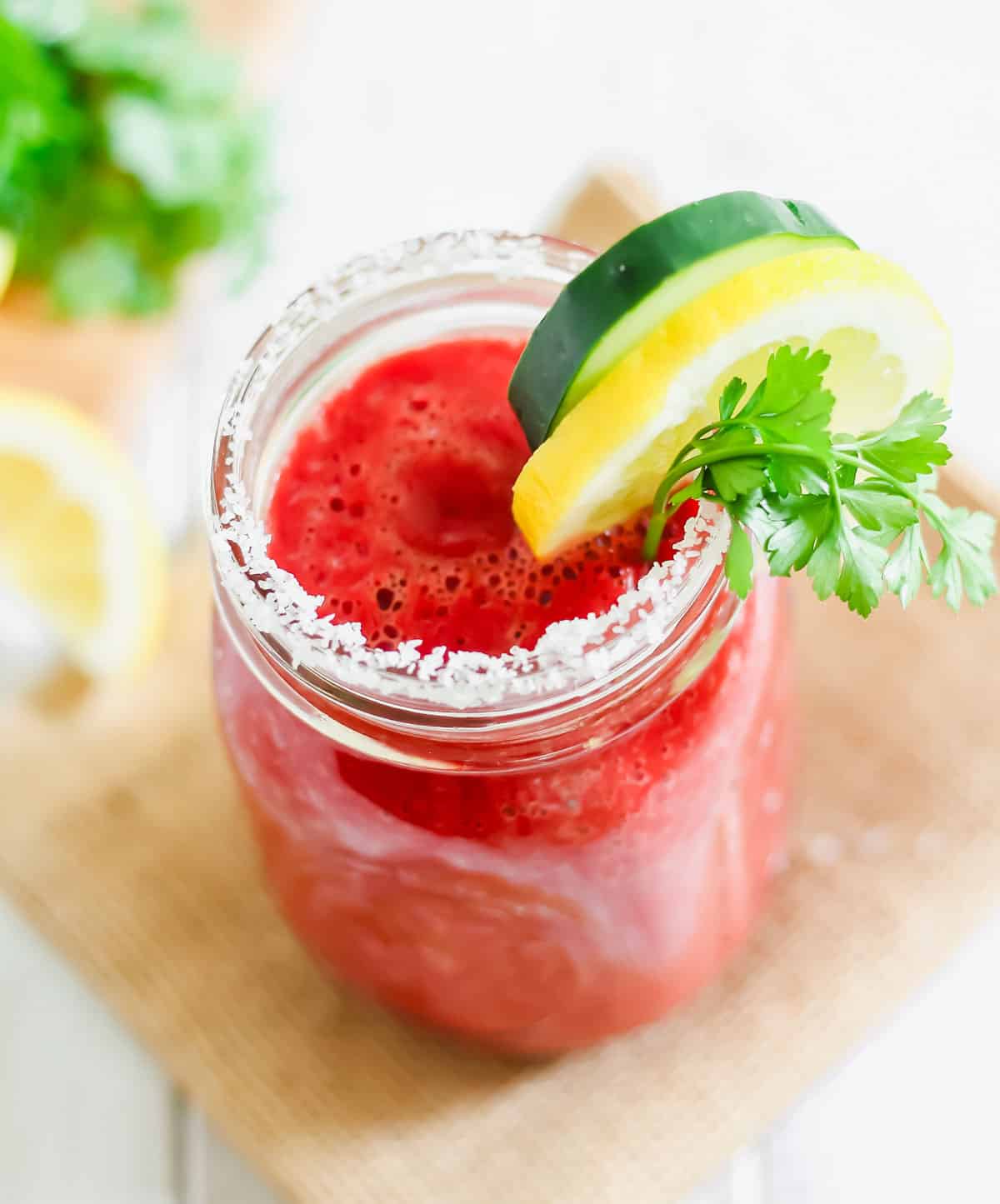 Copycat V8 juice recipe poured into a mason jar lined with salt and garnished with parsley, lemon and cucumber.