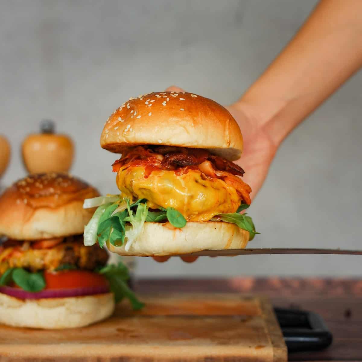 A person is holding a burger on a wooden cutting board.