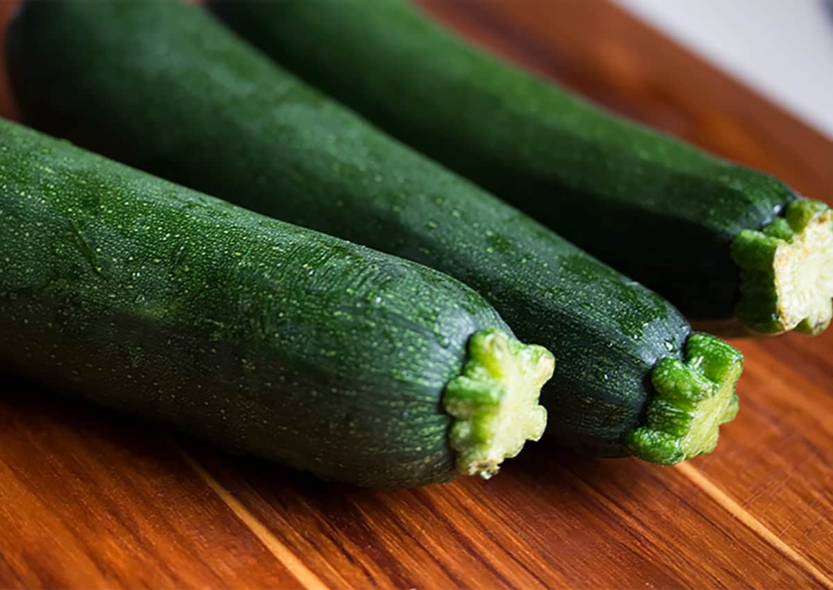 Three green zucchini sitting on a cutting board.