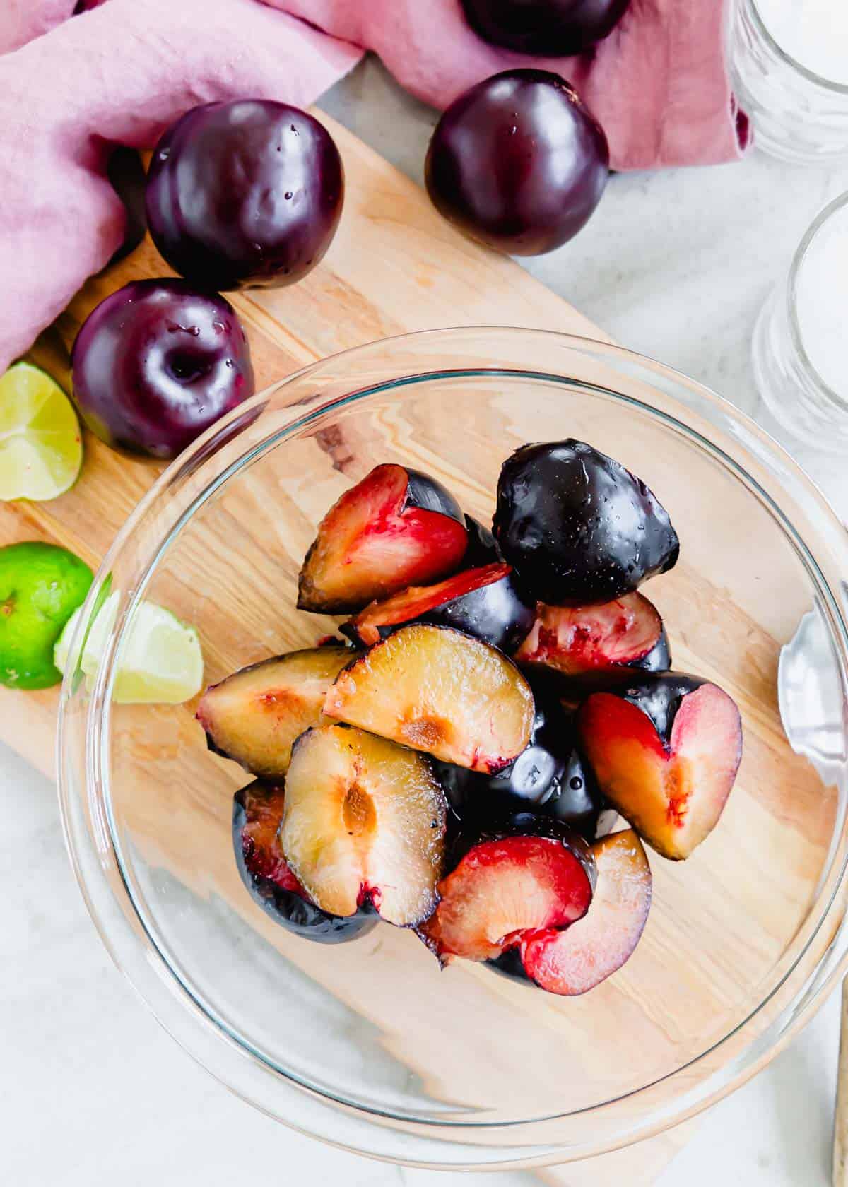 Sliced plums in a bowl on a cutting board.