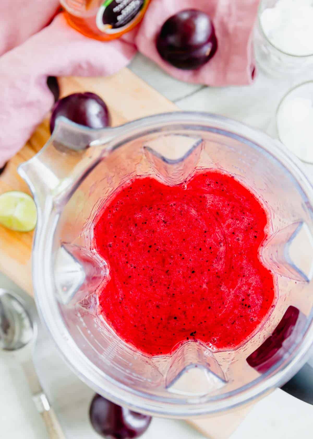 A blender filled with a mixture of plums, lime, honey and water.