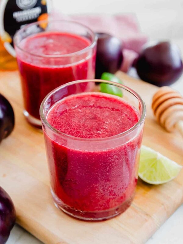 Two glasses of plum juice on a cutting board.