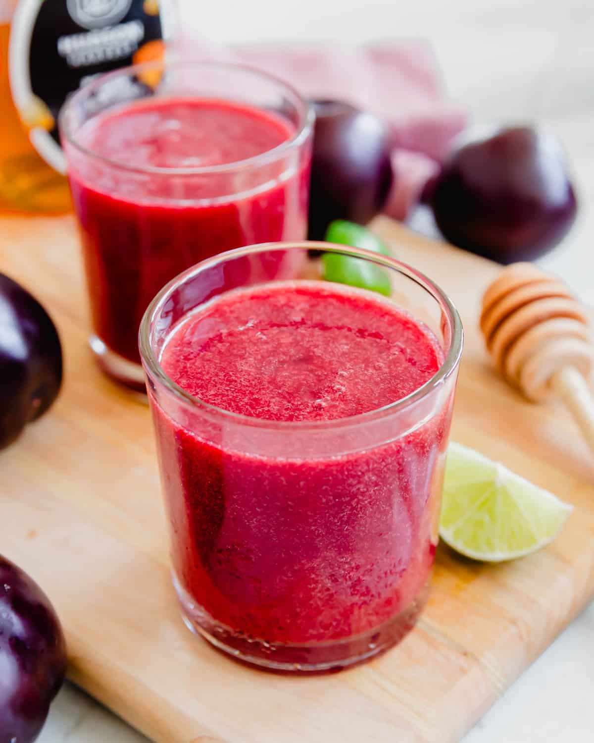 Two glasses of plum juice on a cutting board.