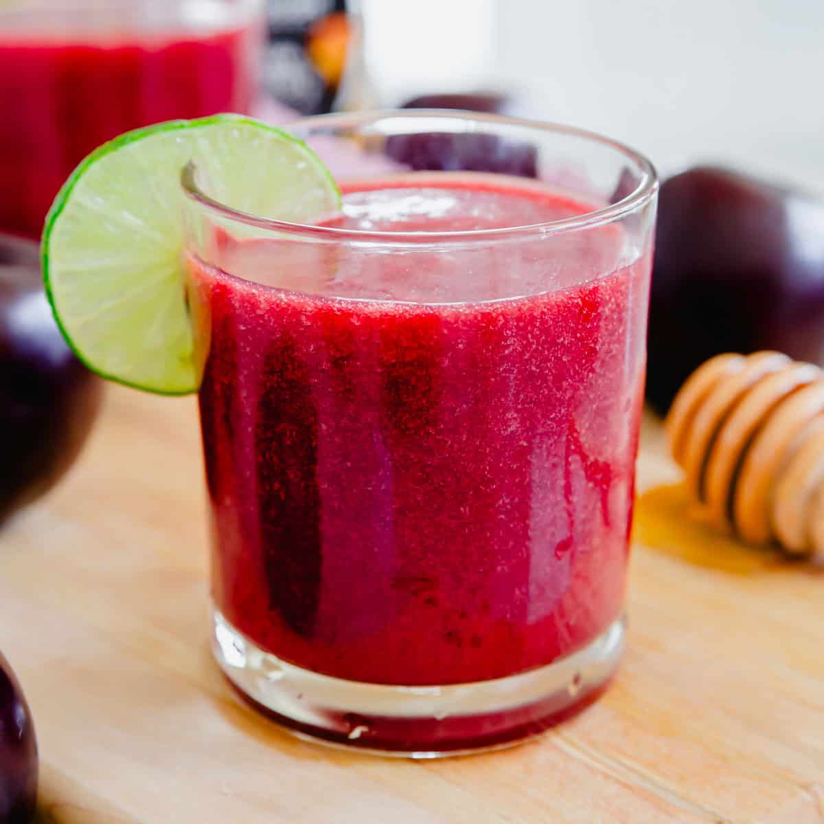 A plum juice drink with a slice of lime on a wooden cutting board.