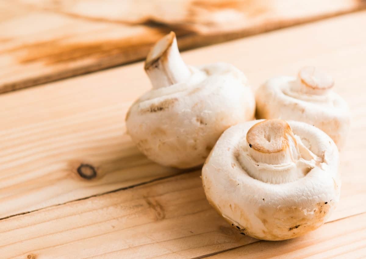 White button mushrooms on a wooden surface.