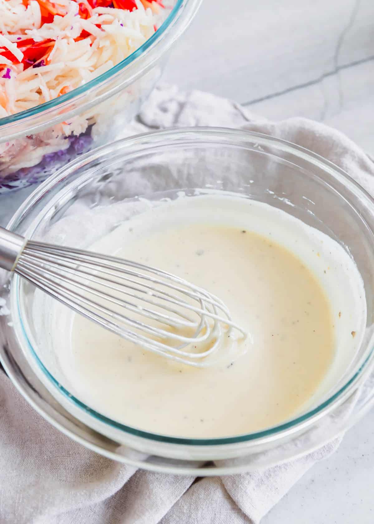 Yogurt based coleslaw dressing in a small glass bowl with a whisk.