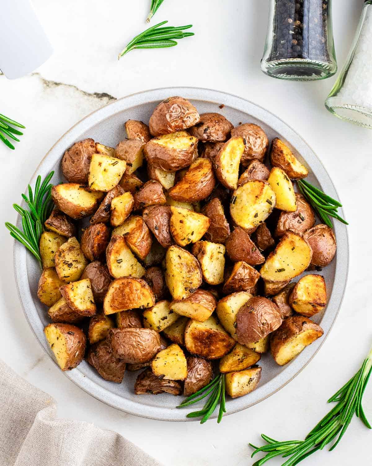 Roasted air fryer red potatoes on a white plate garnished with fresh rosemary.