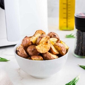 Air fried red potatoes in a white bowl with air fryer in the background.