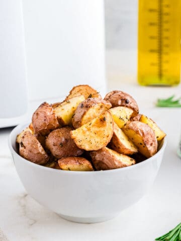 Air fried red potatoes in a white bowl with air fryer in the background.