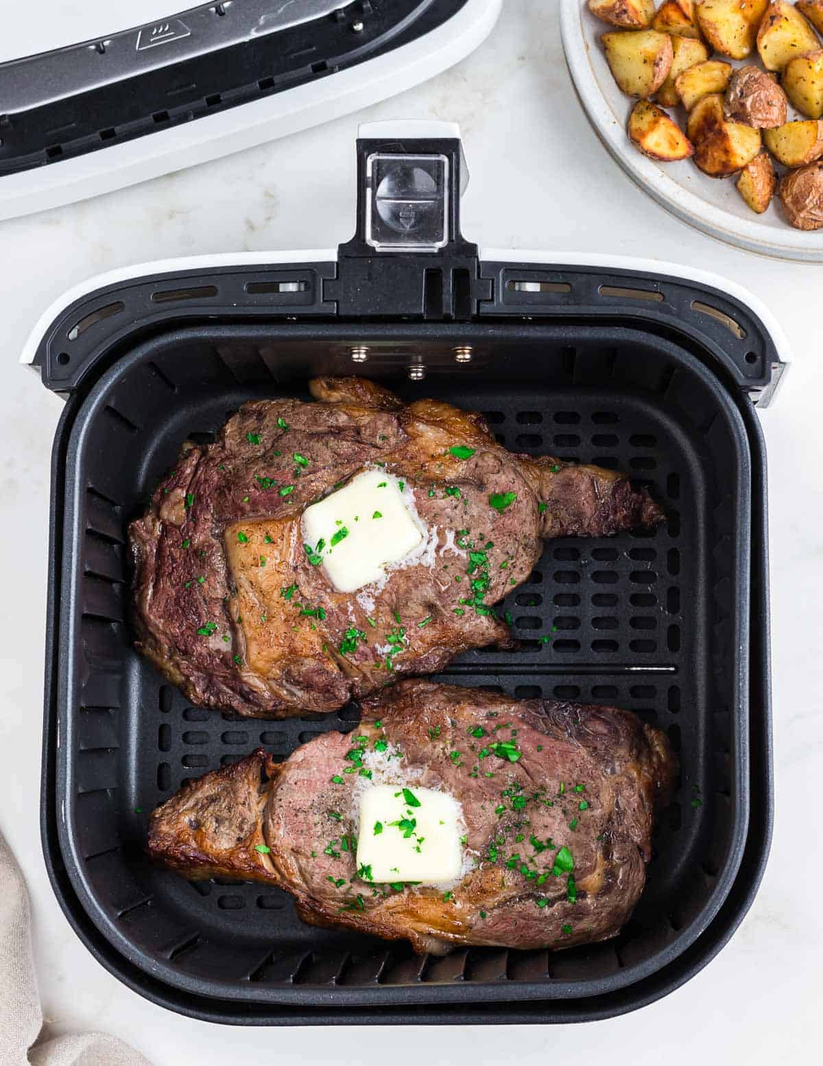 Air fried ribeyes with pats of butter and fresh parsley garnish.