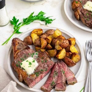 Sliced air fryer ribeye recipe with potatoes on a white plate.