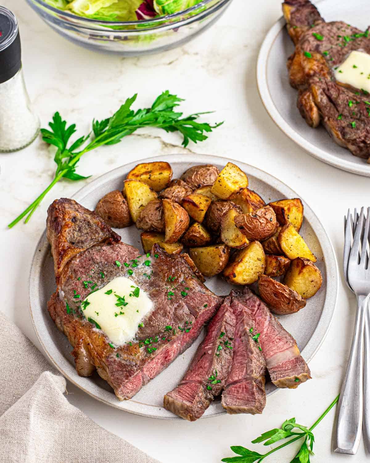 Sliced air fryer ribeye recipe with potatoes on a white plate.