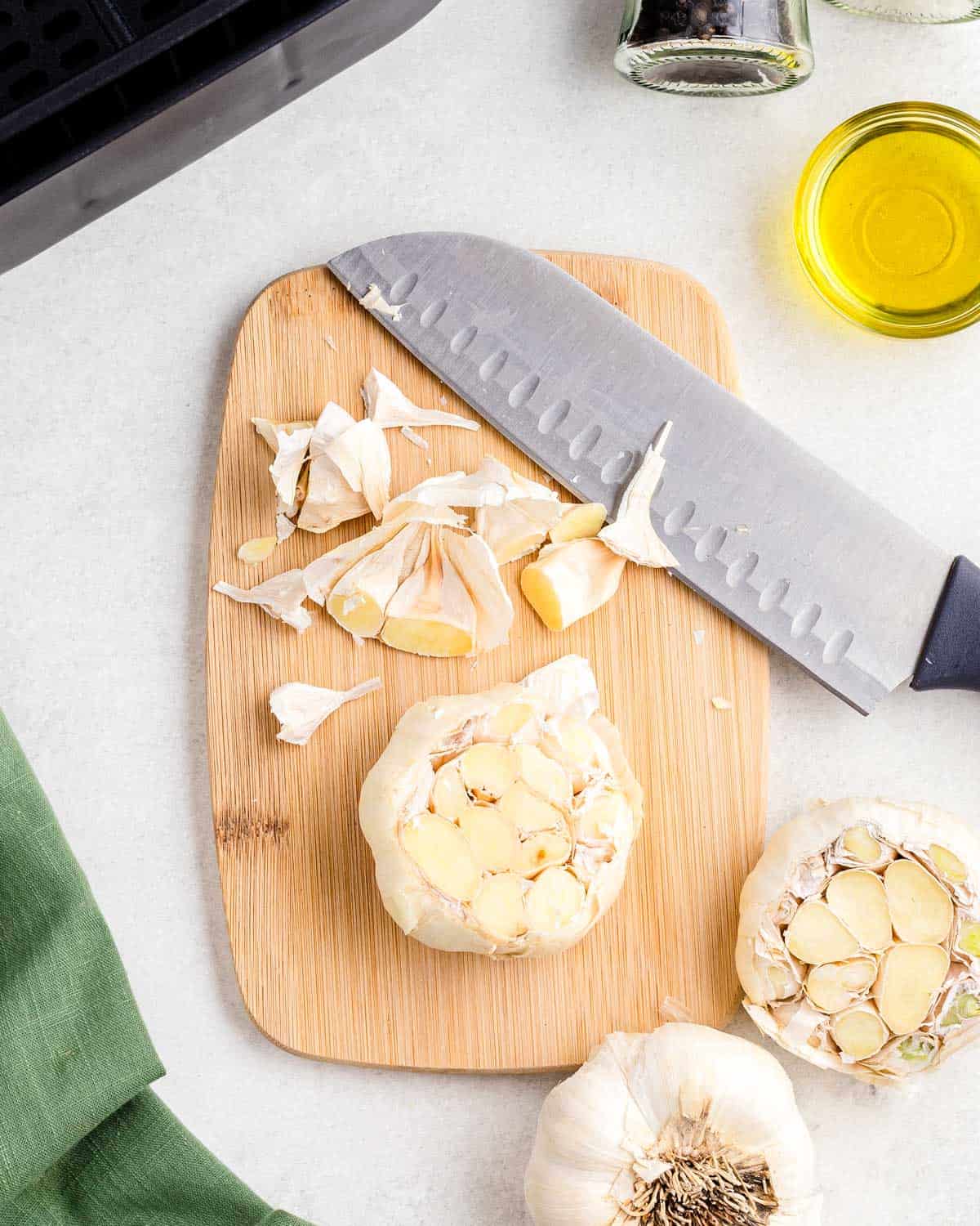 Head of garlic with the top sliced off on a cutting board with a chef's knife.