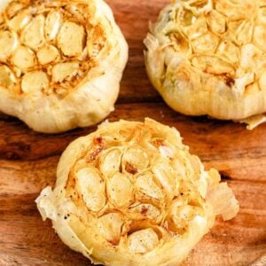 Close up of a head of air fried roasted garlic on a wooden plate.