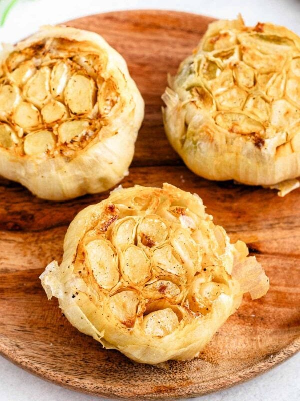 Close up of a head of air fried roasted garlic on a wooden plate.