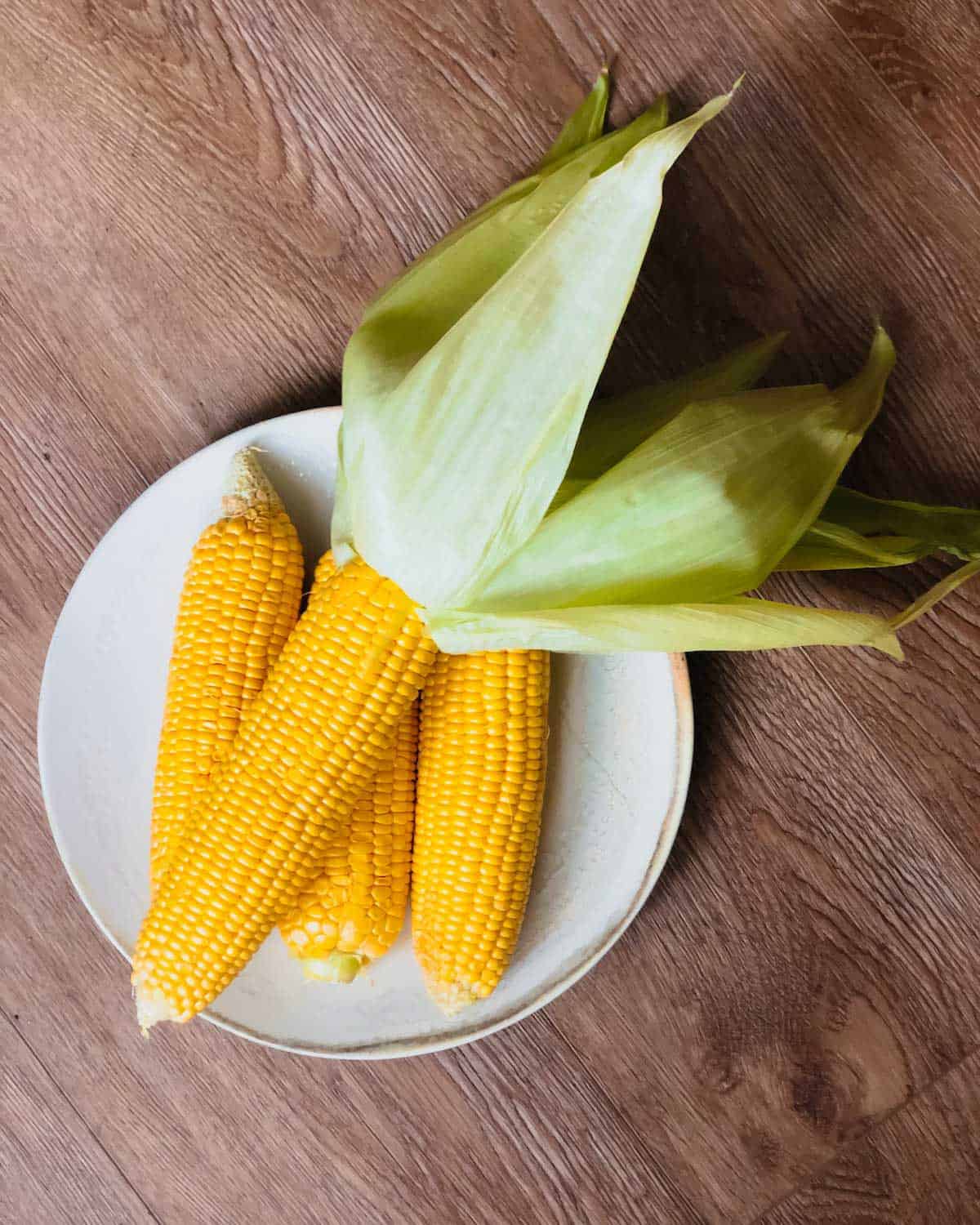Corn on the cob half peeled on a white plate.