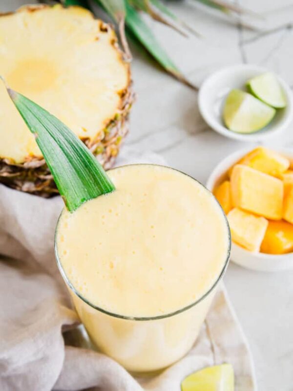 Mango pineapple yogurt smoothie in a glass garnished with a pineapple leaf.