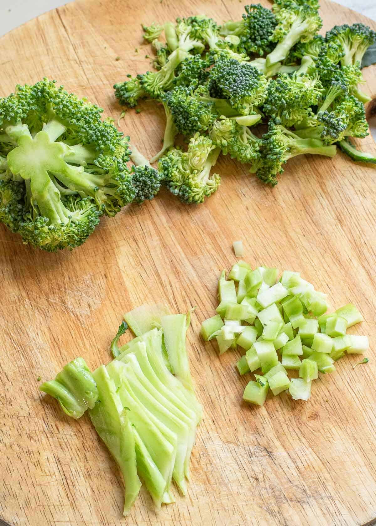 Broccoli stems and florets chopped into different size pieces on a wooden board.