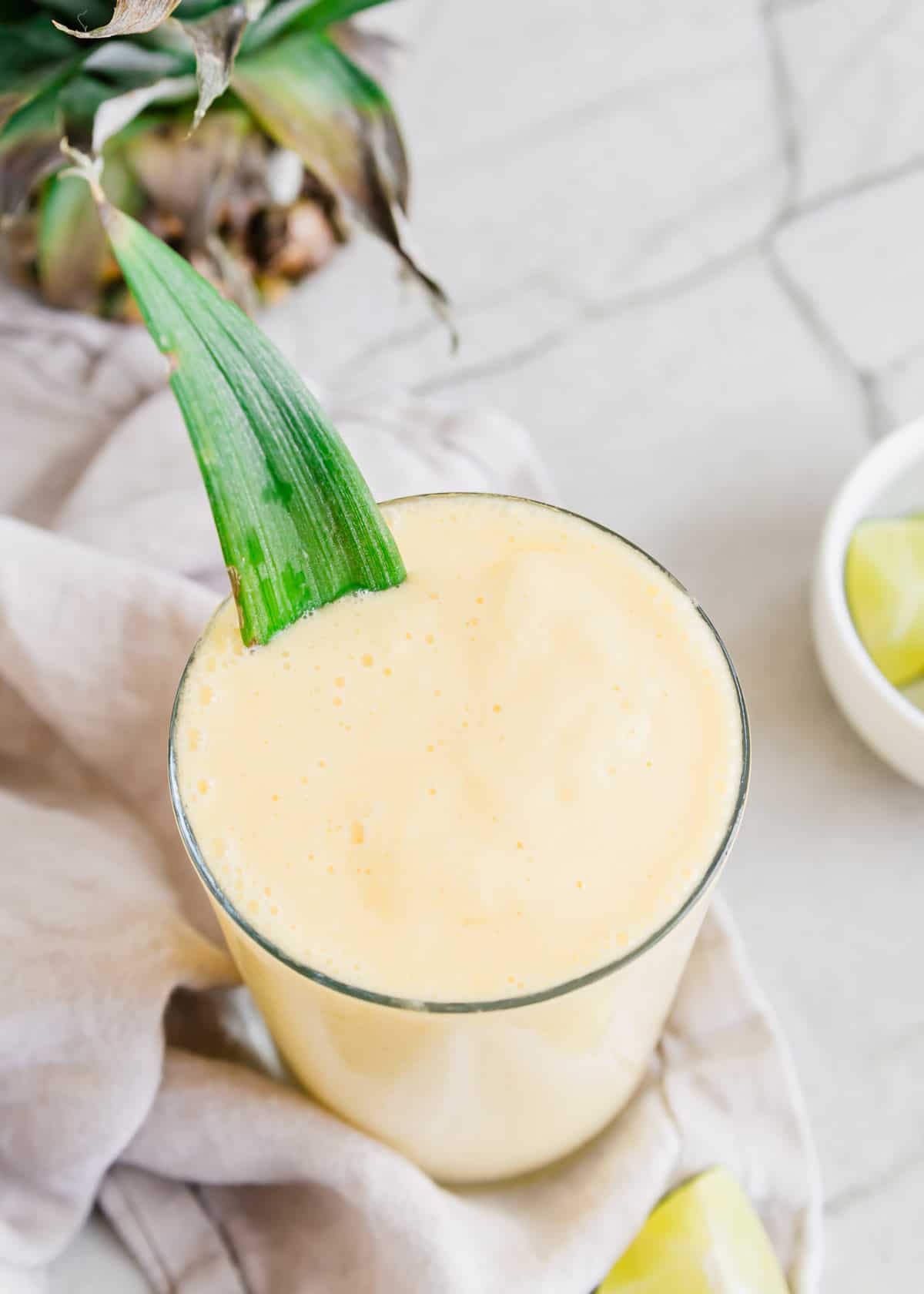 Mango pineapple smoothie in a glass with a pineapple leaf.