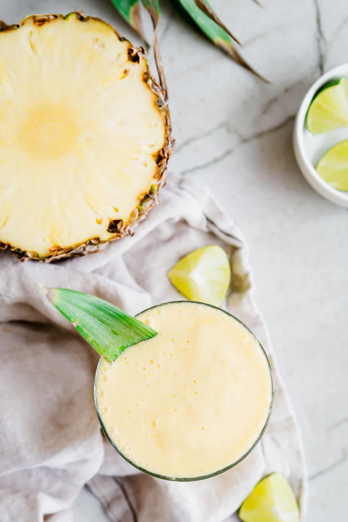 Overhead shot of pineapple mango smoothie with half a pineapple in the background.