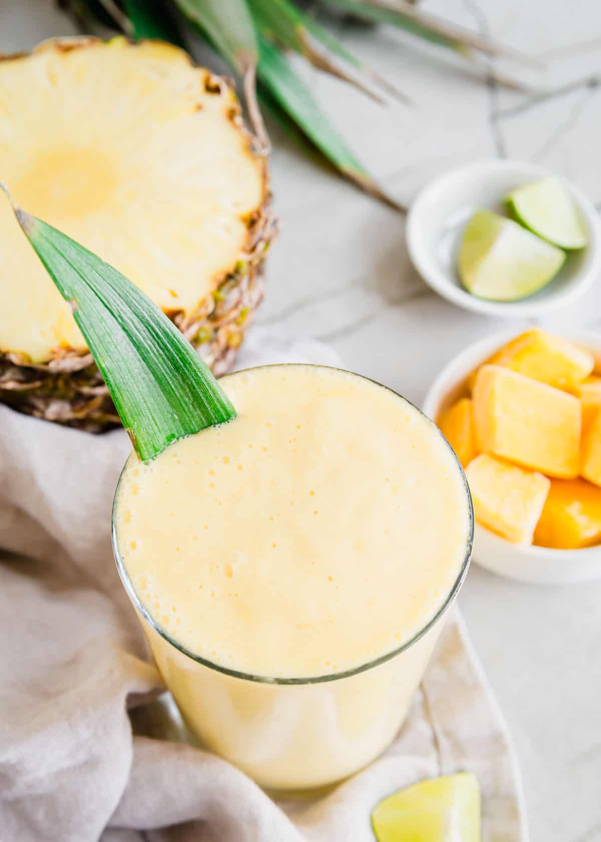 Mango pineapple yogurt smoothie in a glass garnished with a pineapple leaf.