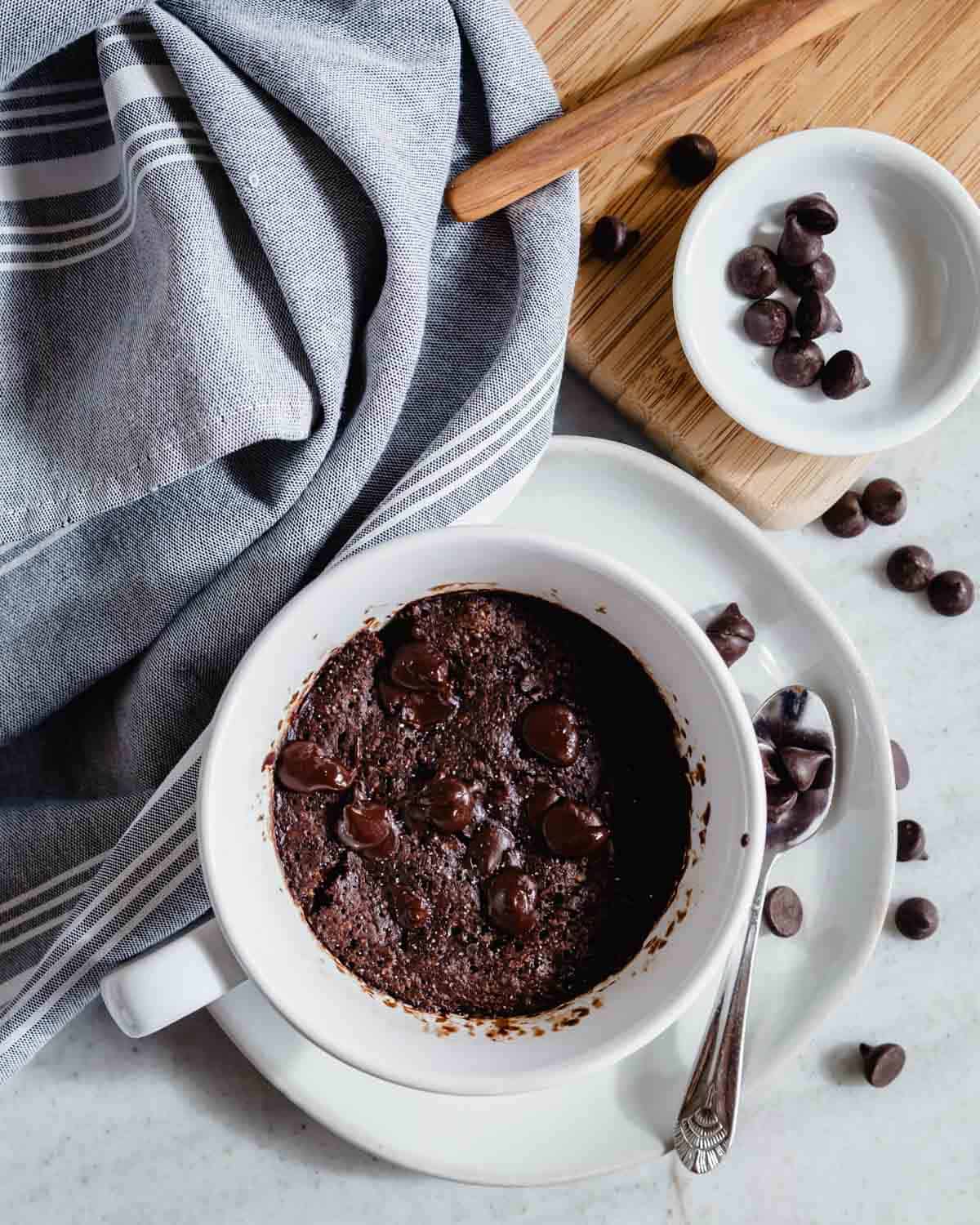 Microwaved chocolate protein mug cake on a dish with chocolate chips scattered around.