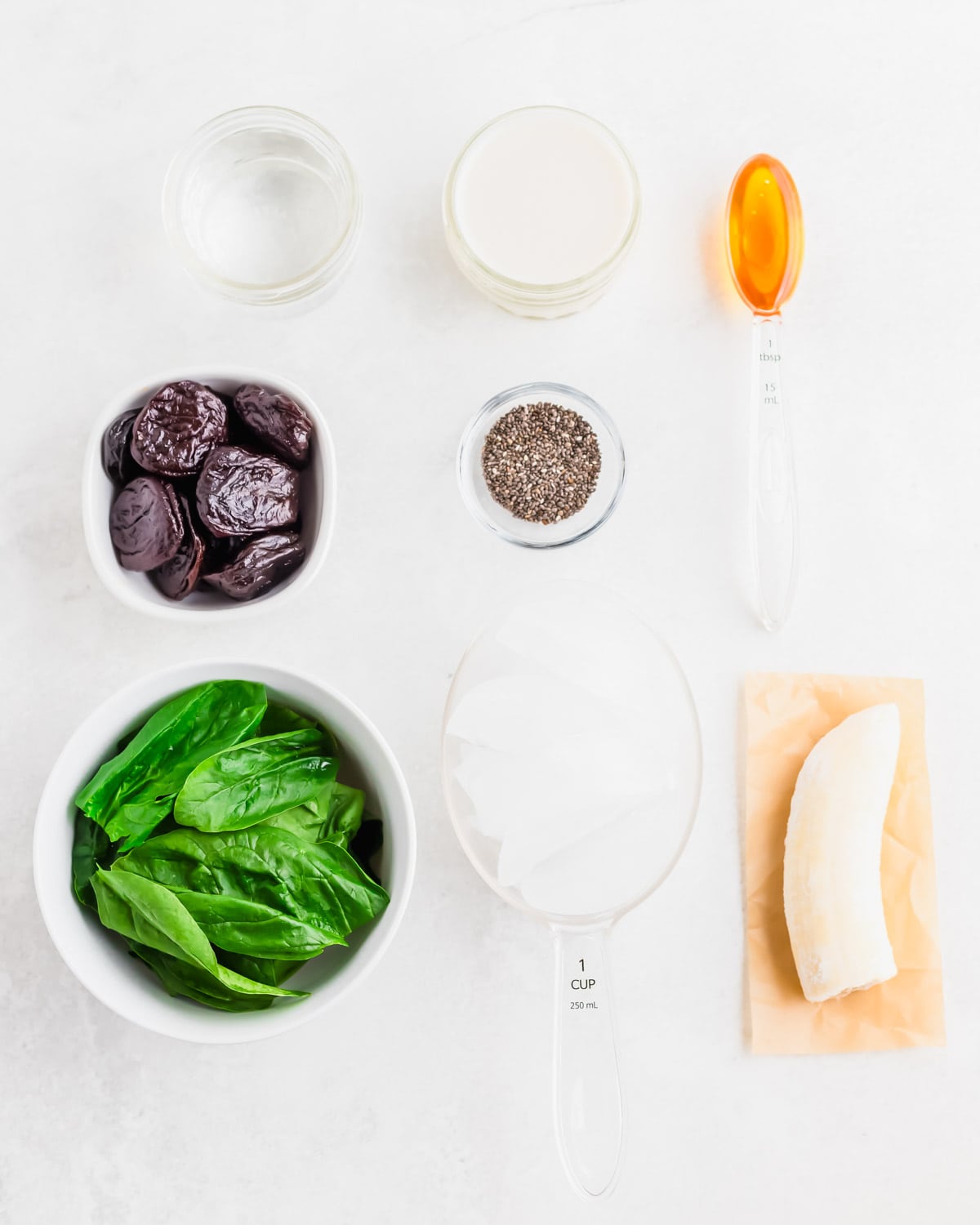Ingredients to make a green prune smoothie on a white surface.