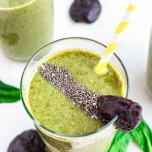 Healthy prune smoothie in a glass with chia seeds, prune garnish and striped yellow and white straw.