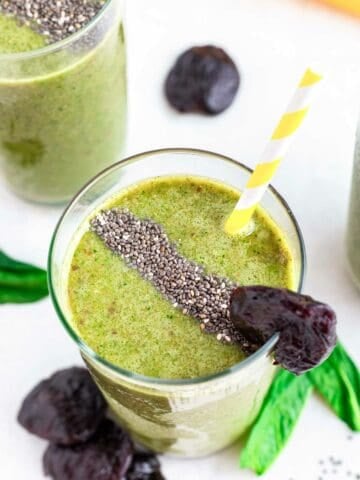 Healthy prune smoothie in a glass with chia seeds, prune garnish and striped yellow and white straw.