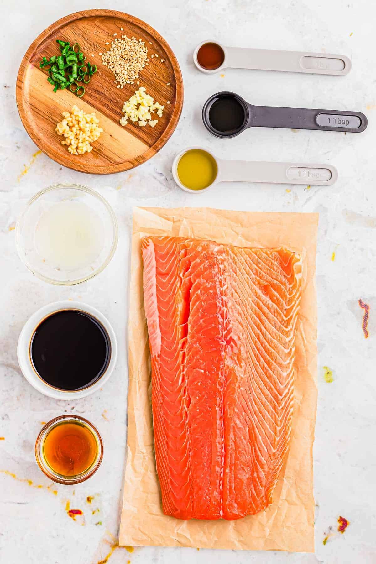 Filet of salmon on parchment paper with marinade ingredients in small bowls and spoons around it.