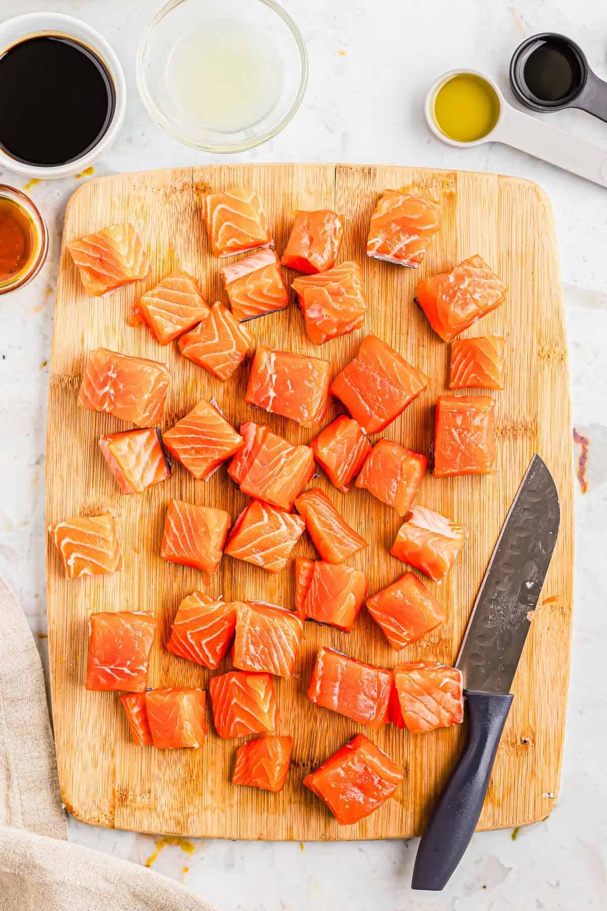 Salmon cut into bite-sized pieces on a wooden cutting board with a knife.