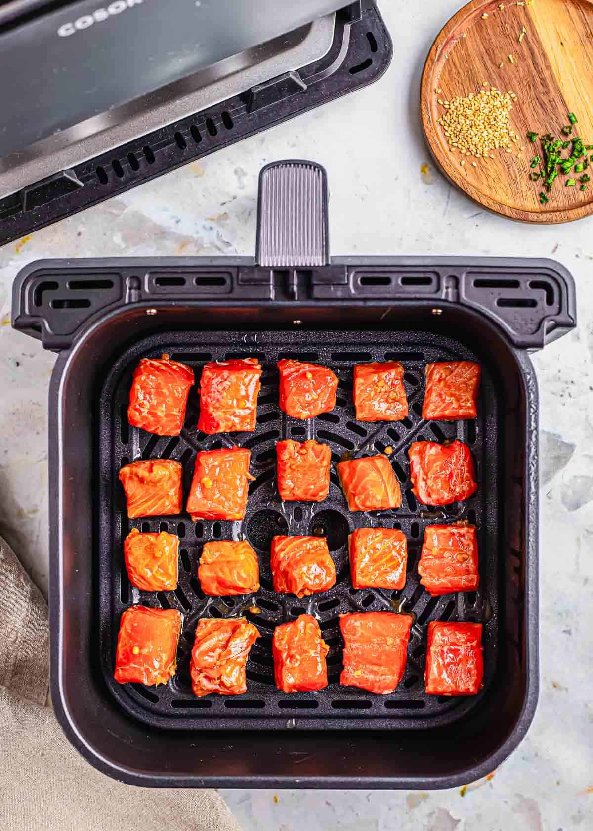 Marinaded salmon bites in the basket of an air fryer.