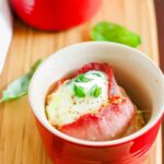 Bacon egg cups with basil on a wooden cutting board.