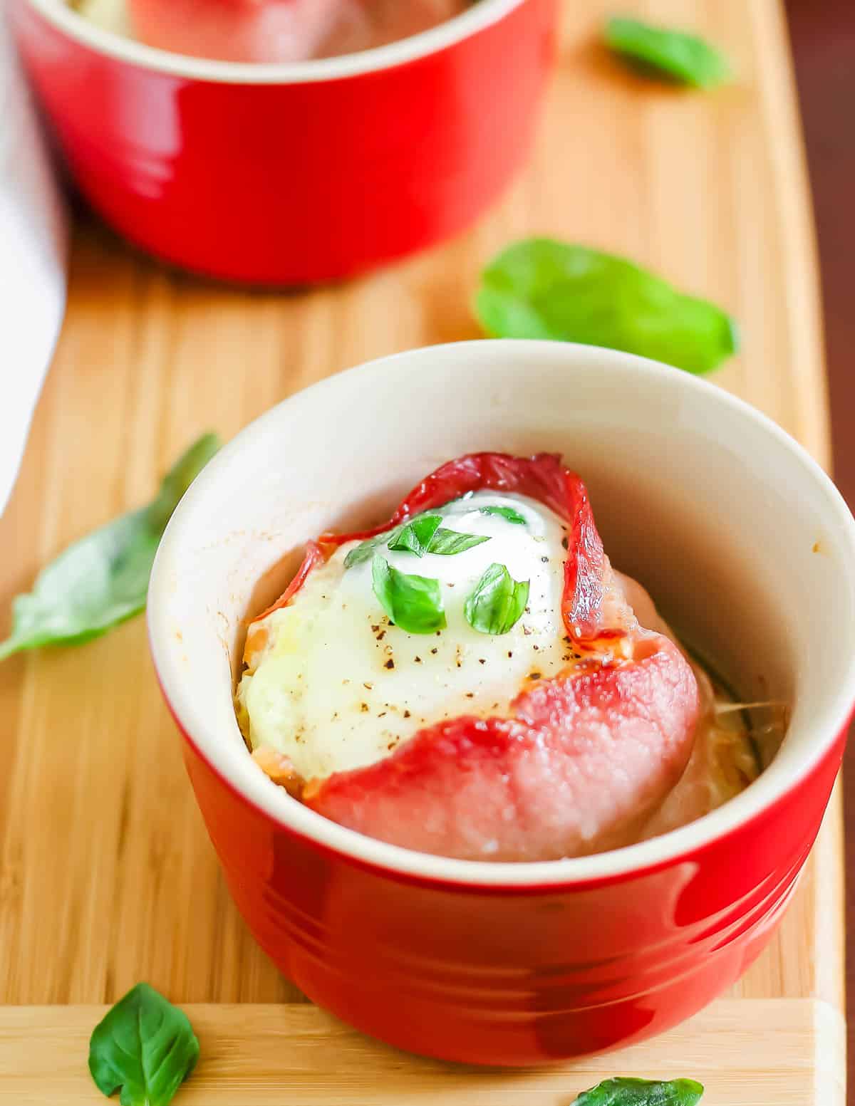 Bacon egg cups with basil on a wooden cutting board.