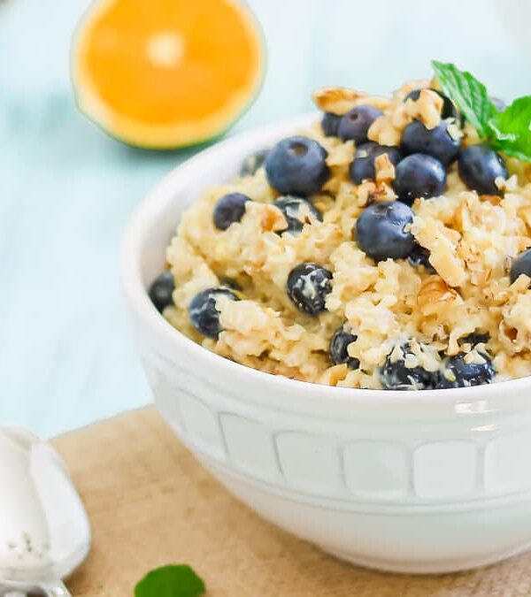 Two white bowls filled with breakfast grains and blueberries garnished with mint leaves.