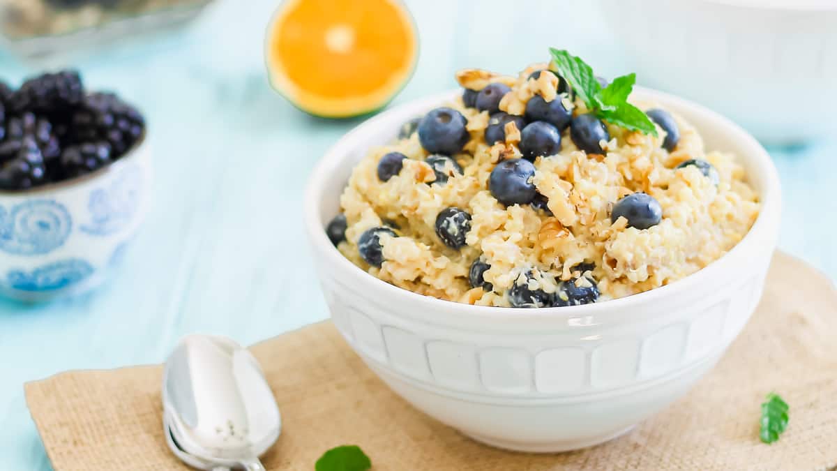 Two white bowls filled with breakfast grains and blueberries garnished with mint leaves.