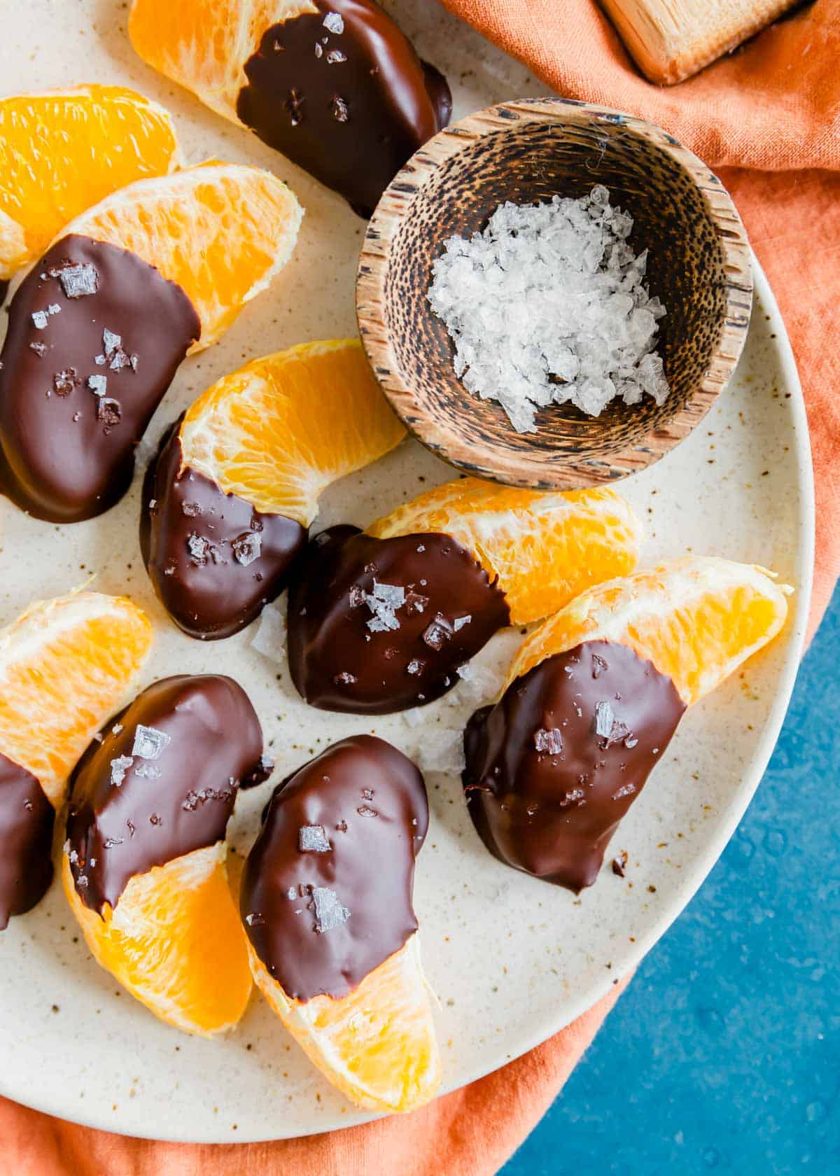 Overhead shot of chocolate orange slices on a plate with small wooden bowl full of flaky salt.