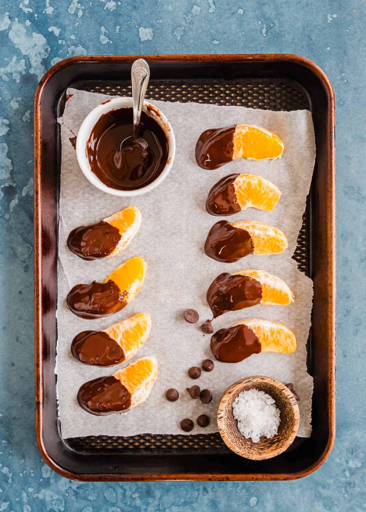 Orange slices dipped in chocolate on parchment paper lined baking sheet.