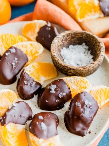 Orange segments half covered in chocolate with coarse salt on a plate.