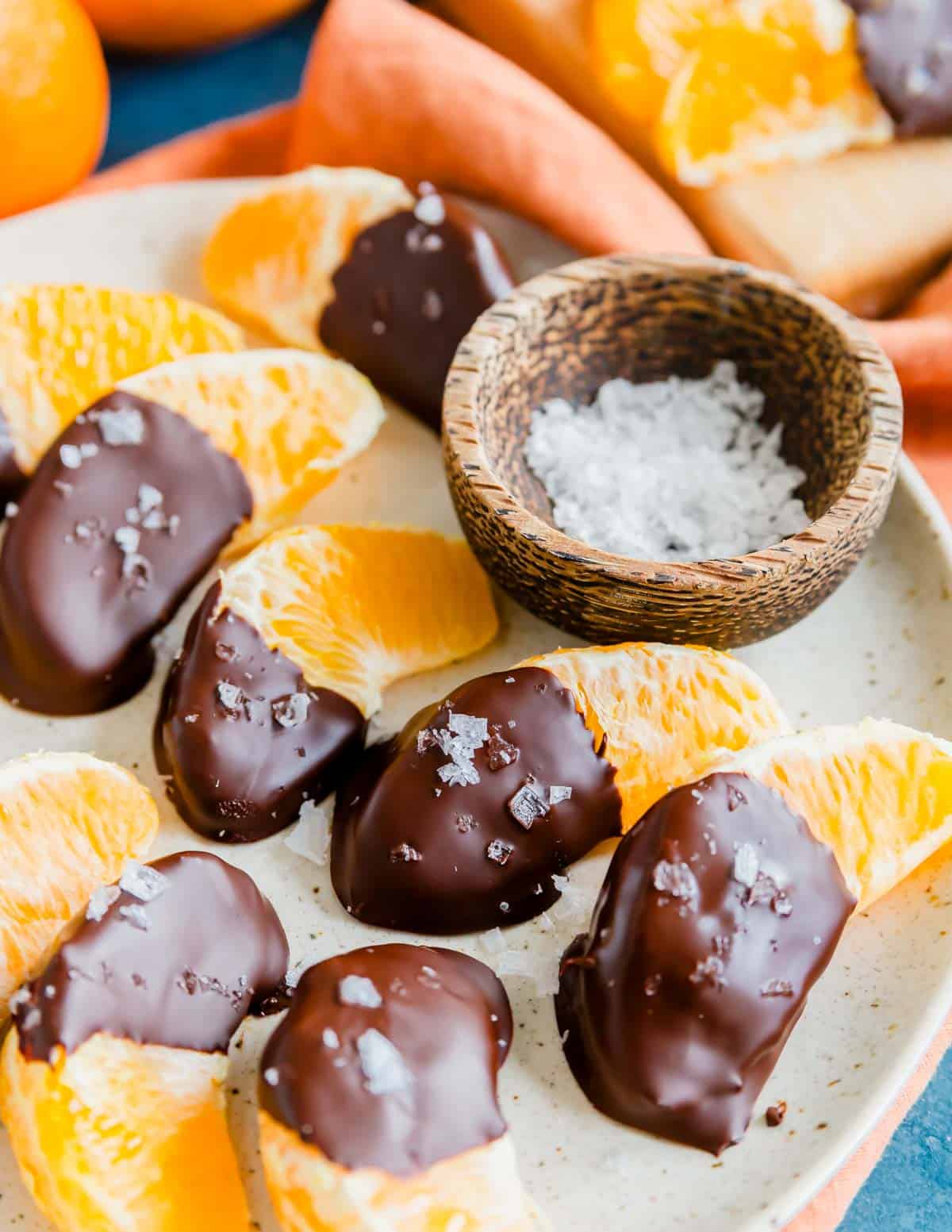 Orange segments half covered in chocolate with coarse salt on a plate.