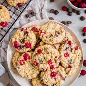 A plate of cranberry and chocolate chip cookies with chocolate chips and fresh cranberries scattered around it.