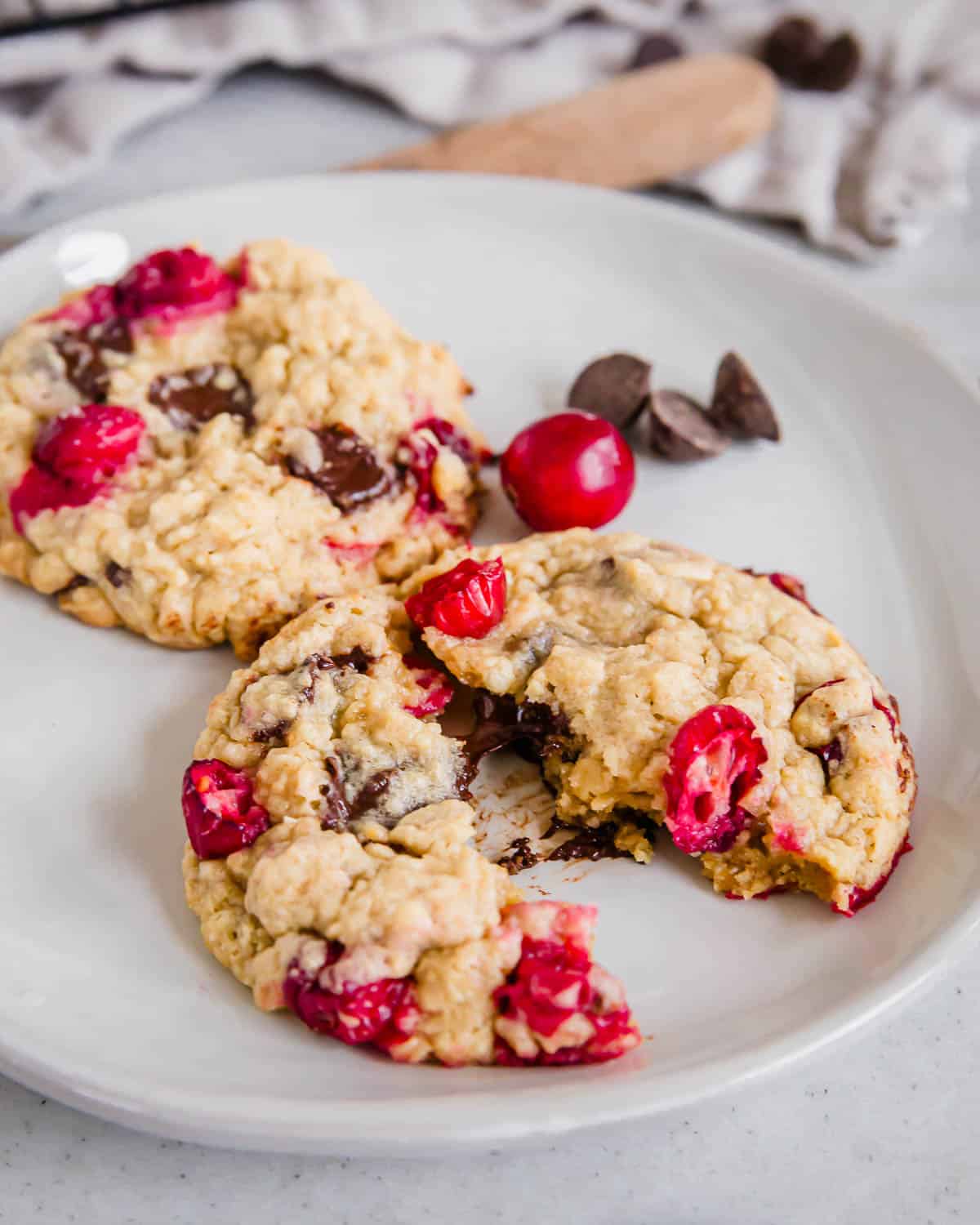 Two cranberry chocolate chip cookies on a plate with one split on half.
