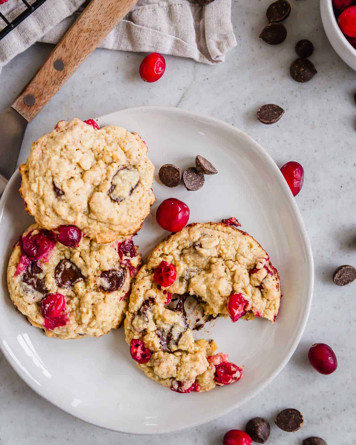 Fresh cranberry cookies with chocolate chips on a plate with a metal cookie spatula next to it.